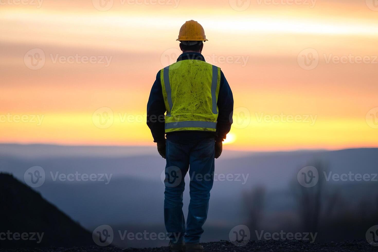 Construction worker observing sunset over hills while wearing safety gear in a rural landscape at dusk photo