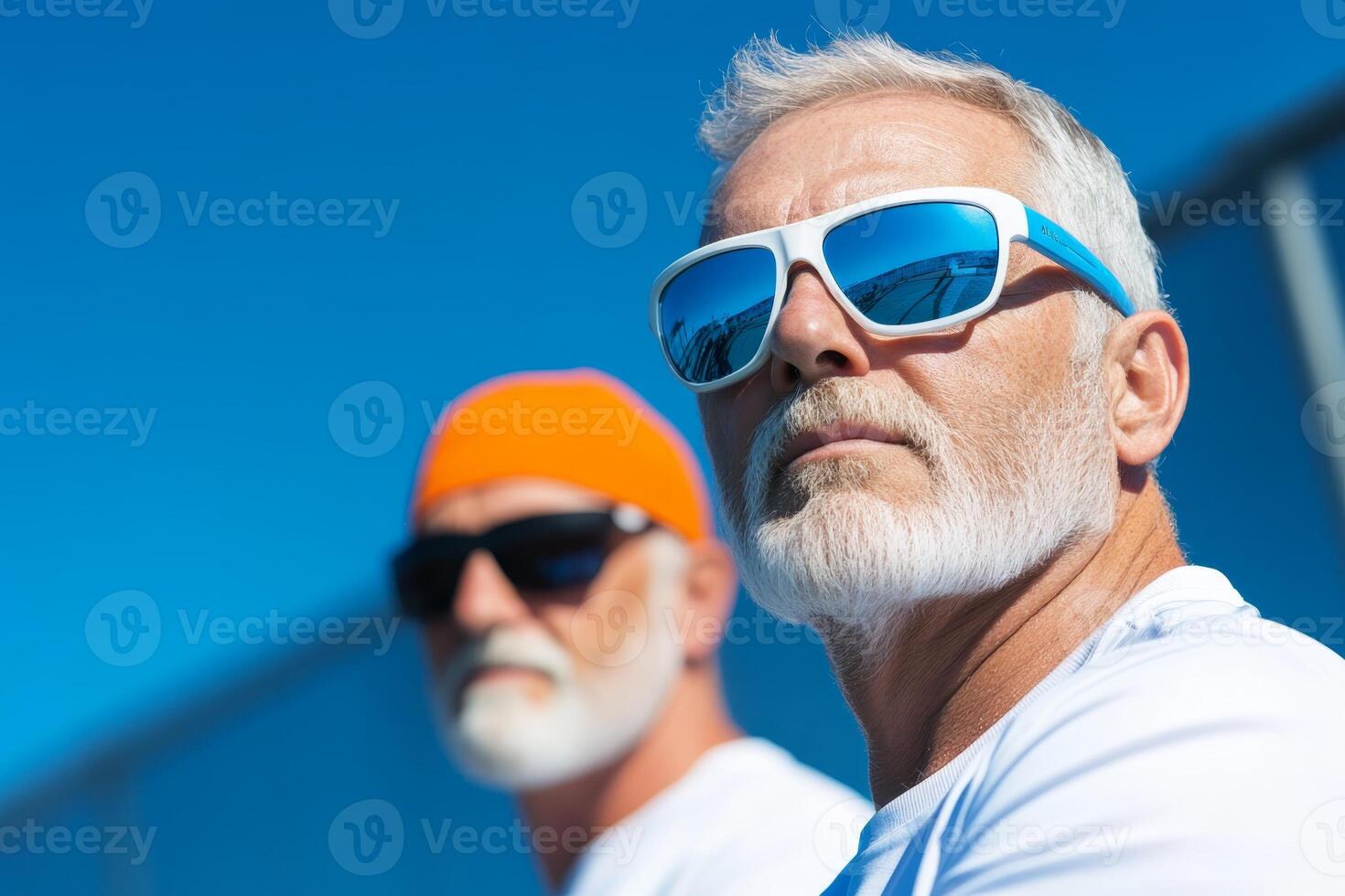 Two elderly men wearing sunglasses and colorful caps enjoying a sunny day outdoors at the beach during summer photo