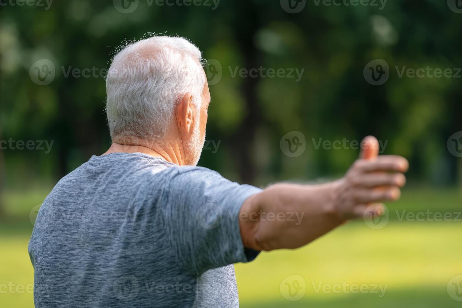 Elderly man enjoying a sunny day while stretching in a green park setting during the afternoon hours photo