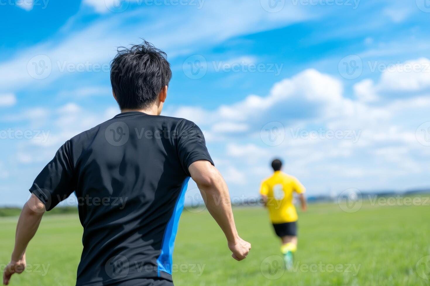 Two young men running on a green field under a bright blue sky in a friendly competition photo