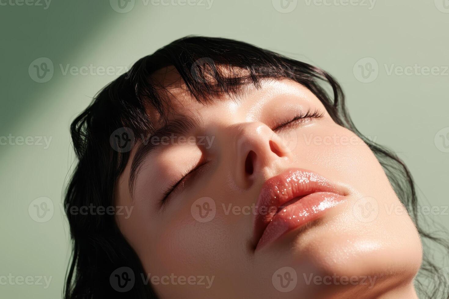 Close-up of a serene woman with closed eyes, showcasing glowing skin against a green background during daylight hours photo