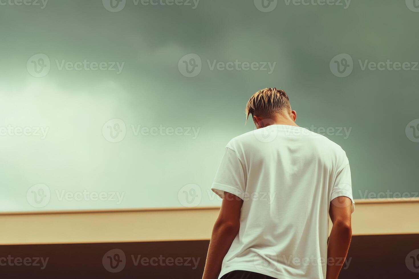 Young man stands with back to camera, gazing at cloudy sky over an urban landscape in late afternoon light photo