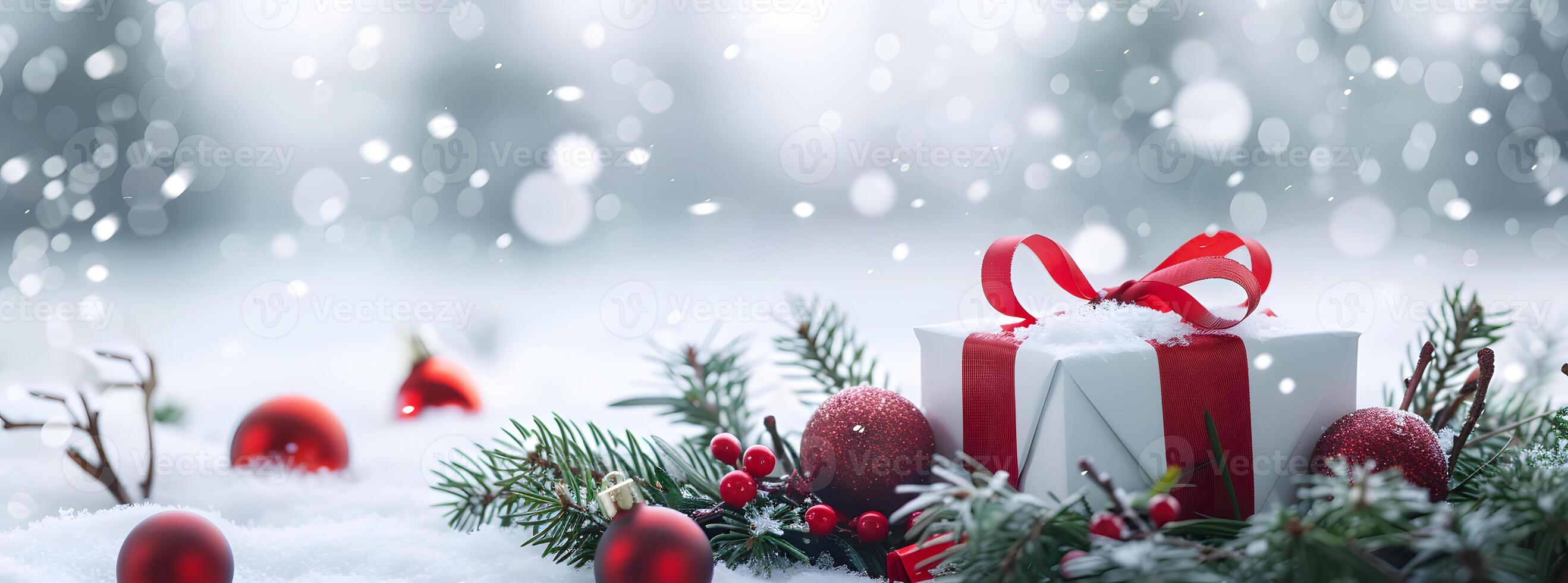 Gift box with a red ribbon and bow, surrounded by green pine branches and red Christmas ornaments, resting on fresh snow for a festive holiday scene photo