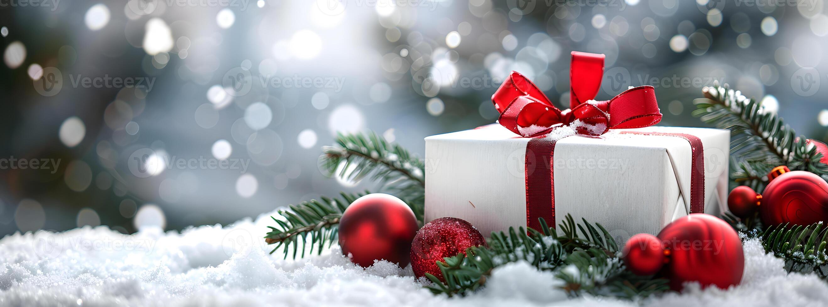 gift box wrapped with red ribbon and bow, surrounded by green pine branches and ornaments on soft snow, creating a festive winter setting photo