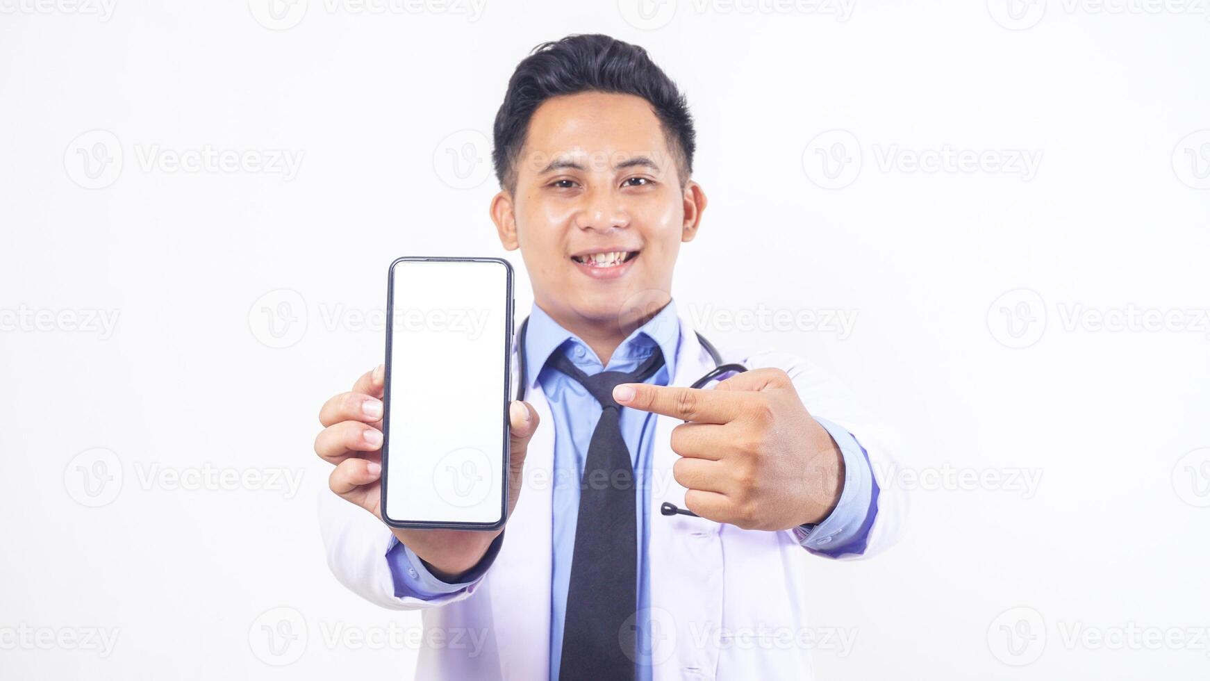Portrait of Handsome Asian Male Doctor Pointing at Mobile Phone with Blank Screen Mock Up on White Background photo