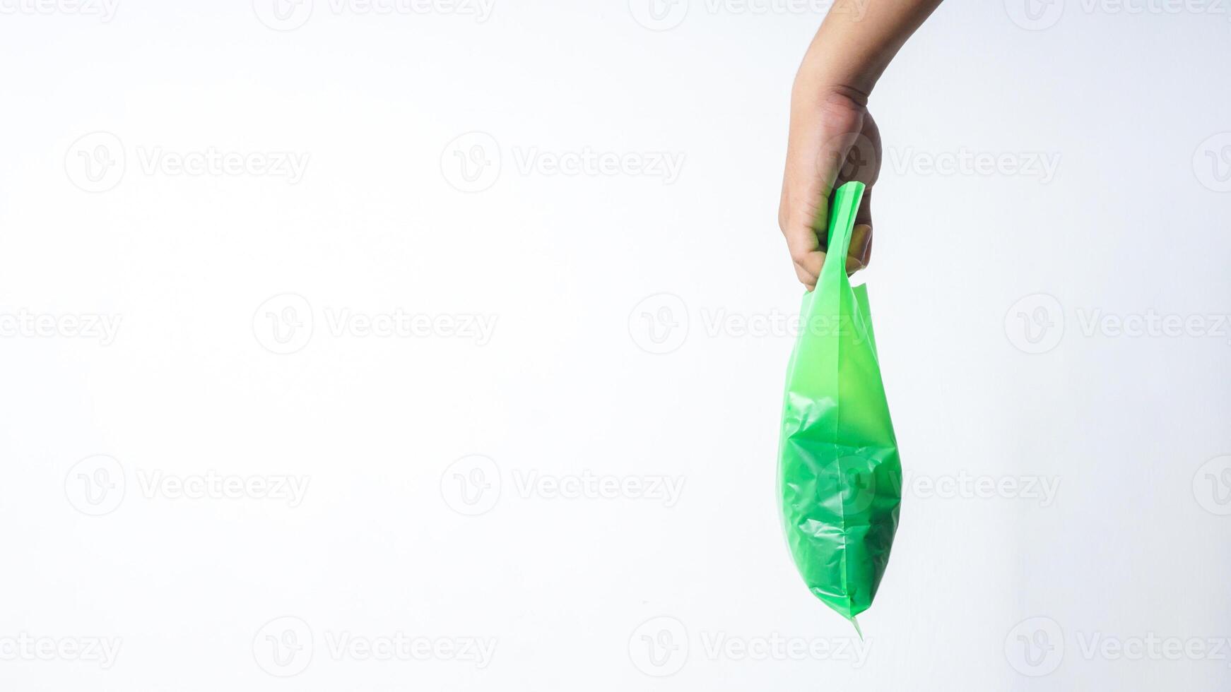 Side View of Hand Carrying Green Plastic Grocery Bag with Copy Space on White Background photo