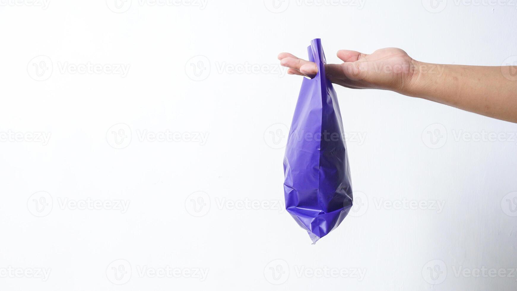 Side View of Hand Carrying Filled Purple Plastic Bag on White Background photo