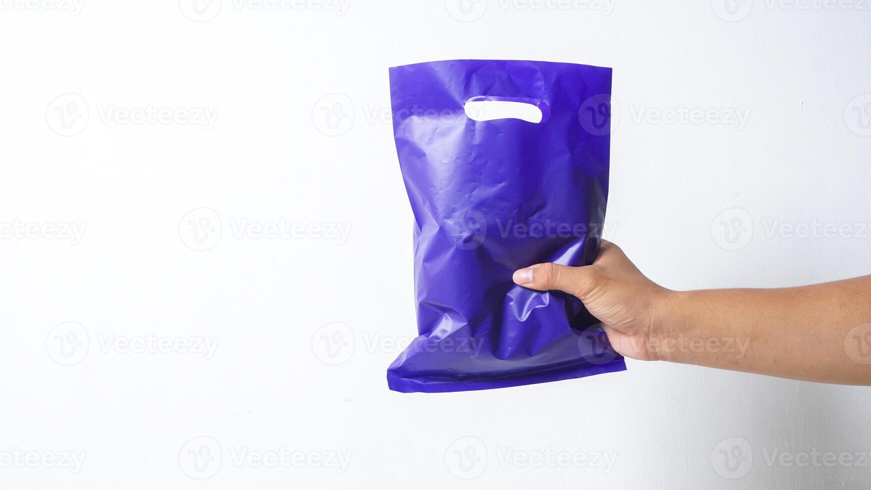 Hand Holding Filled Purple Plastic Bag Mock Up with Copy Space on White Background photo