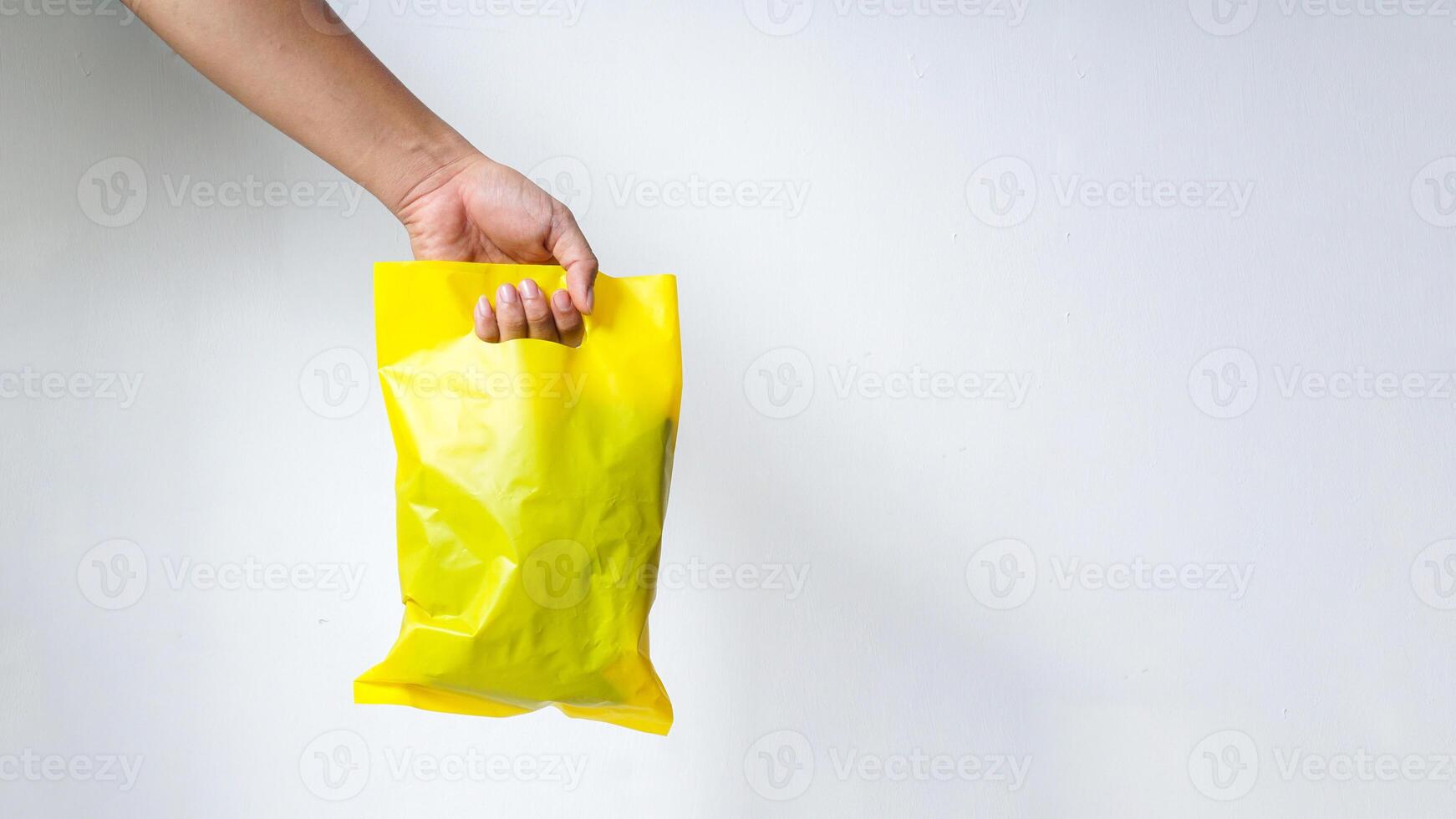 Hand Carrying Filled Yellow Plastic Bag with Copy Space on White Background photo