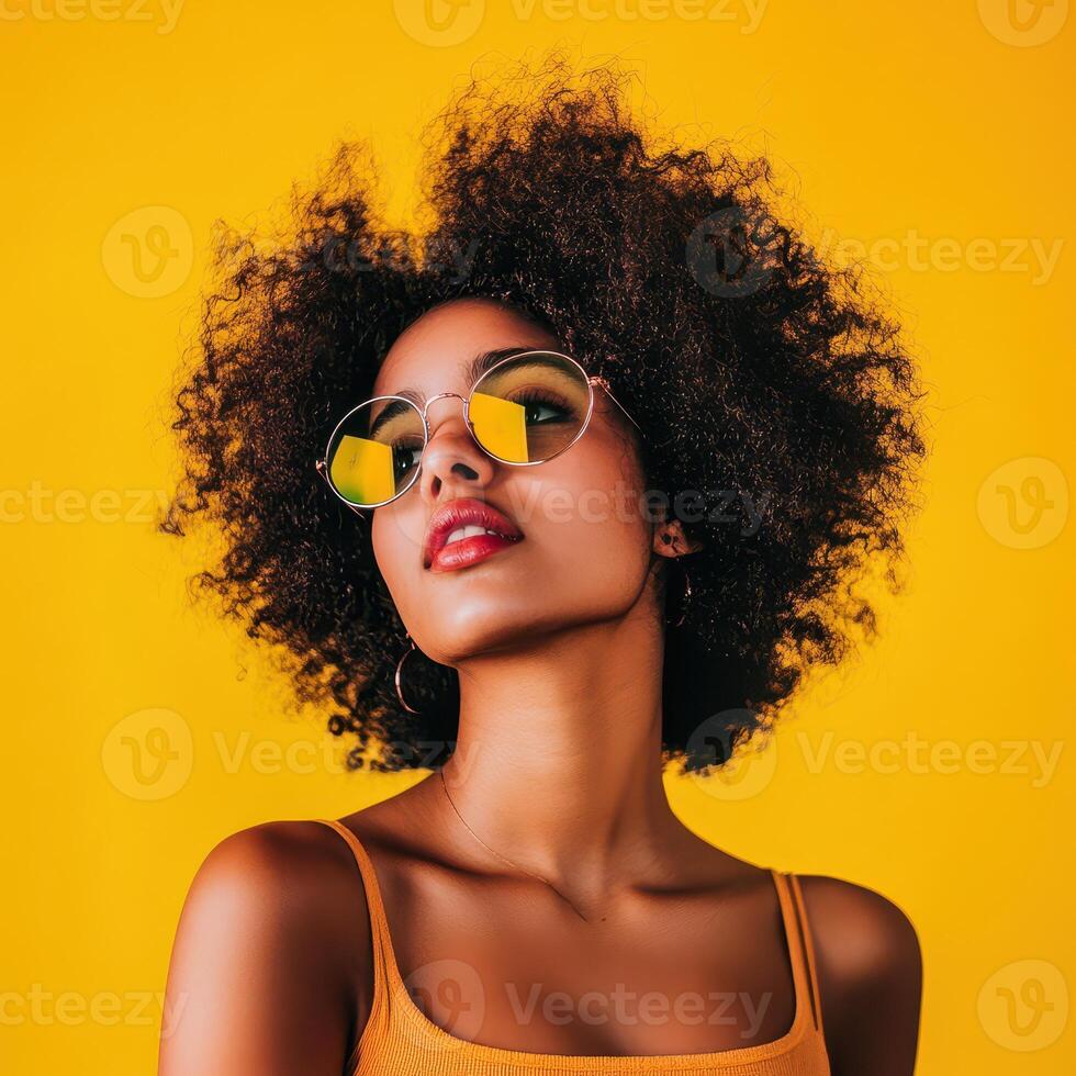 Beautiful african american woman wearing sunglasses and posing against a yellow background photo
