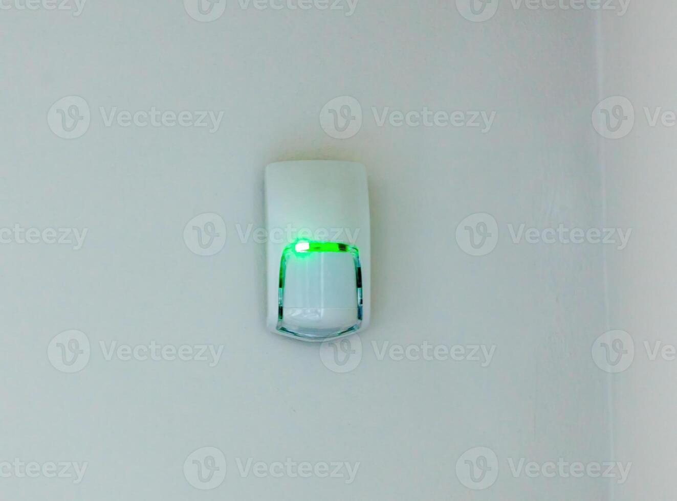 Security alarm motion sensor flashing green light on white wall photo