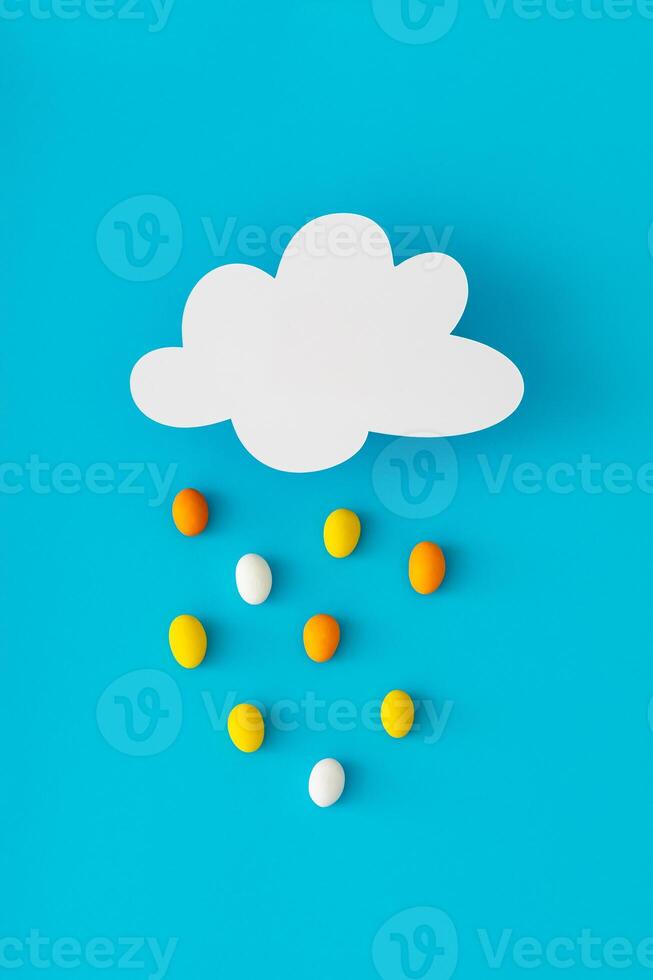Creative composition made of cloud shape paper card note and colorful Easter eggs rain on blue background. Minimal Easter concept. Festive holiday layout. Easter aesthetic. Flat lay style. Top view. photo