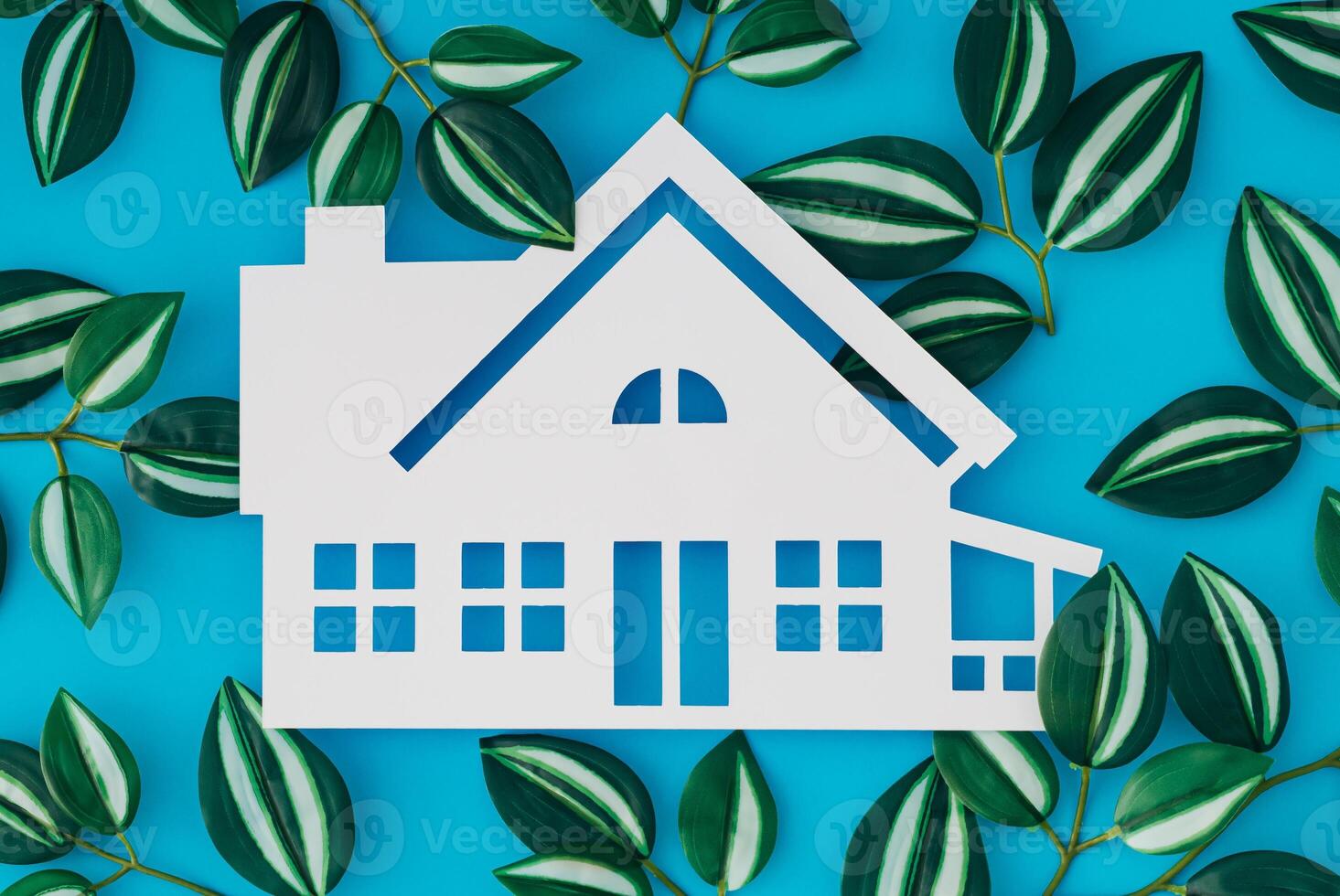 House shaped white paper cutout and colorful leaves on light blue background. Minimal concept. Flat lay style. Top view banner. photo