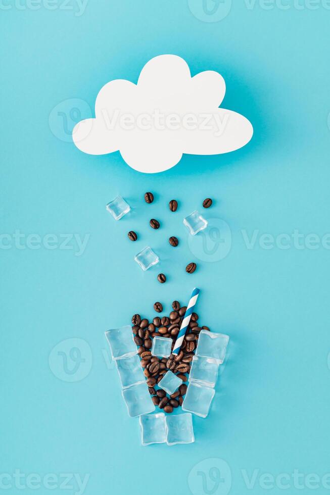 Cloud shape paper card note and rain and cup of coffee made of coffee beans and ice cubes on blue background. Creative weather minimal concept. Coffee aesthetic. Unique flat lay. photo