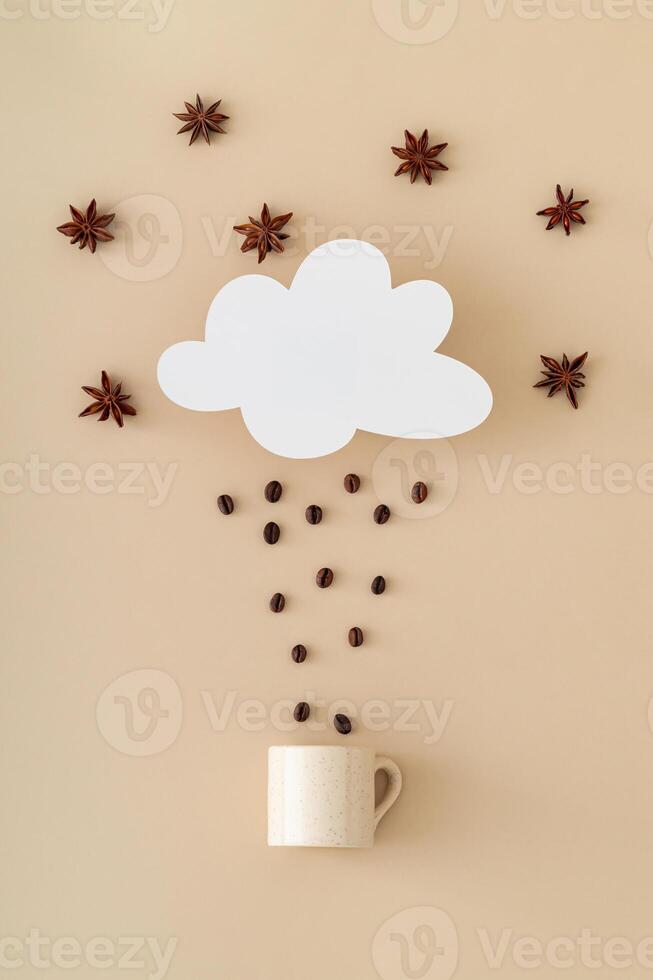 Creative layout made of cloud shape paper card note, coffee beans rain, star anise and coffee cup on beige background. Minimal concept. Trendy weather idea. Coffee aesthetic. Flat lay style. photo