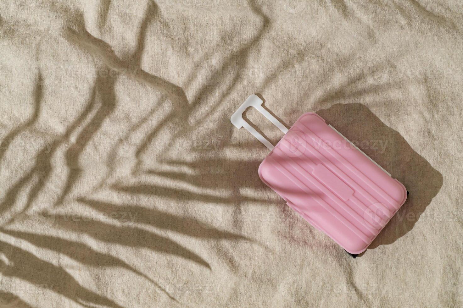 Summer day scene with tropical palm tree leaf shadow and pastel pink baggage on sand color linen background. Minimal stylish travel concept. Trendy summertime adventure idea. Flat lay, top view. photo