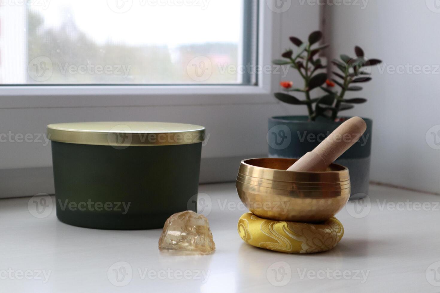 A gold singing bowl and a gold candle sit on a table photo