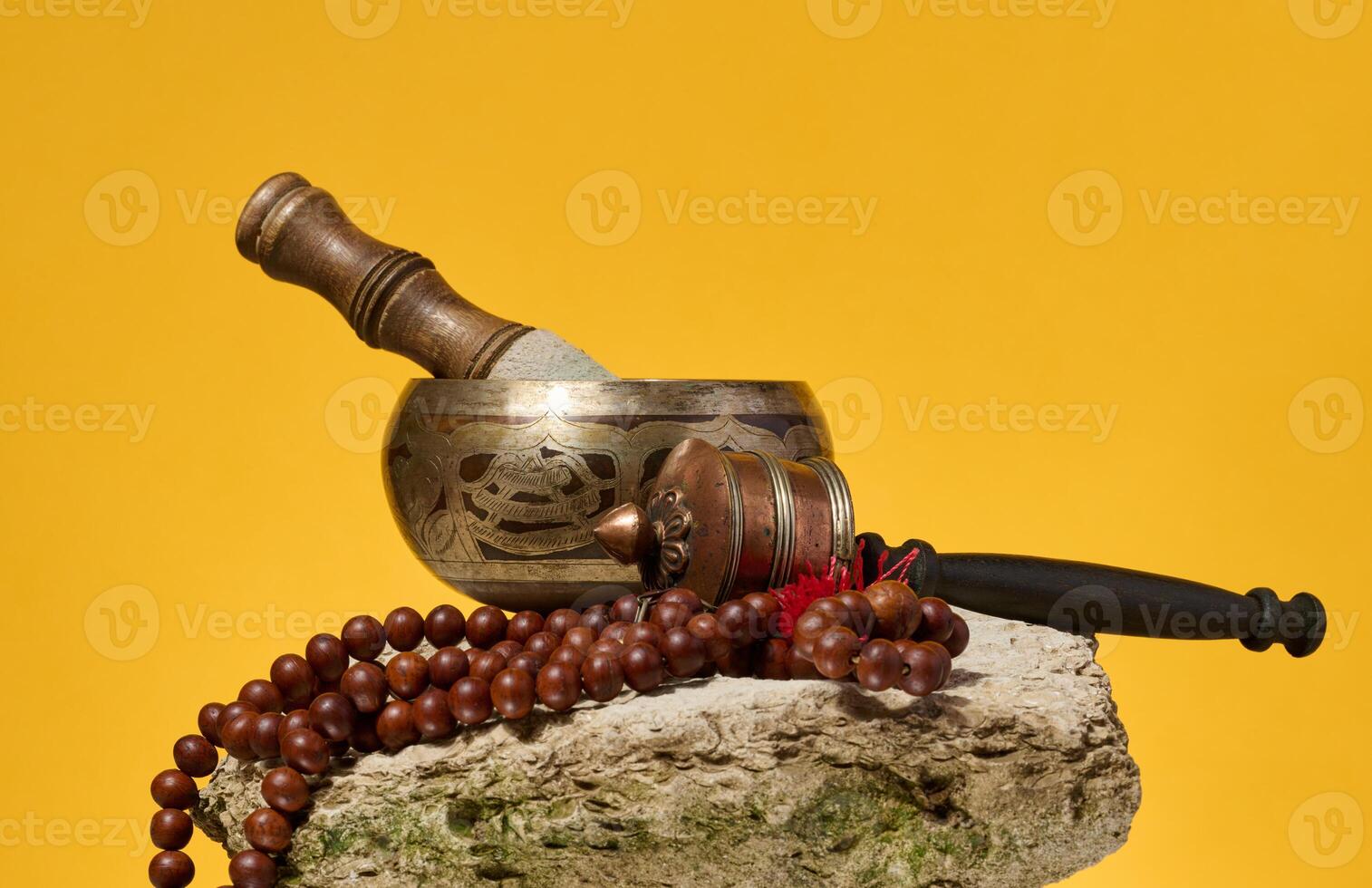 Copper singing bowl, wooden stick and prayer beads on stone, yellow background photo