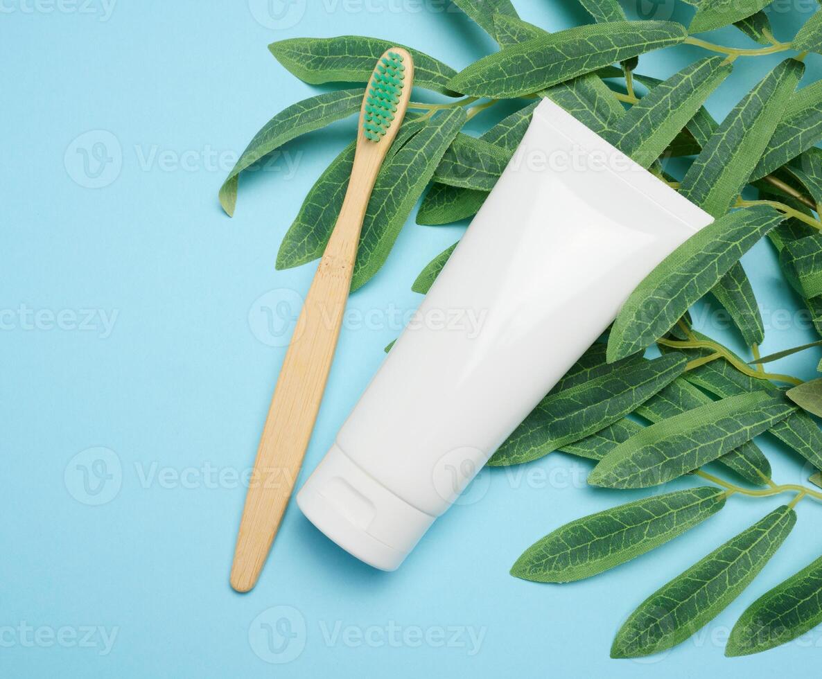 White plastic tube and bamboo toothbrush on blue background, top view photo