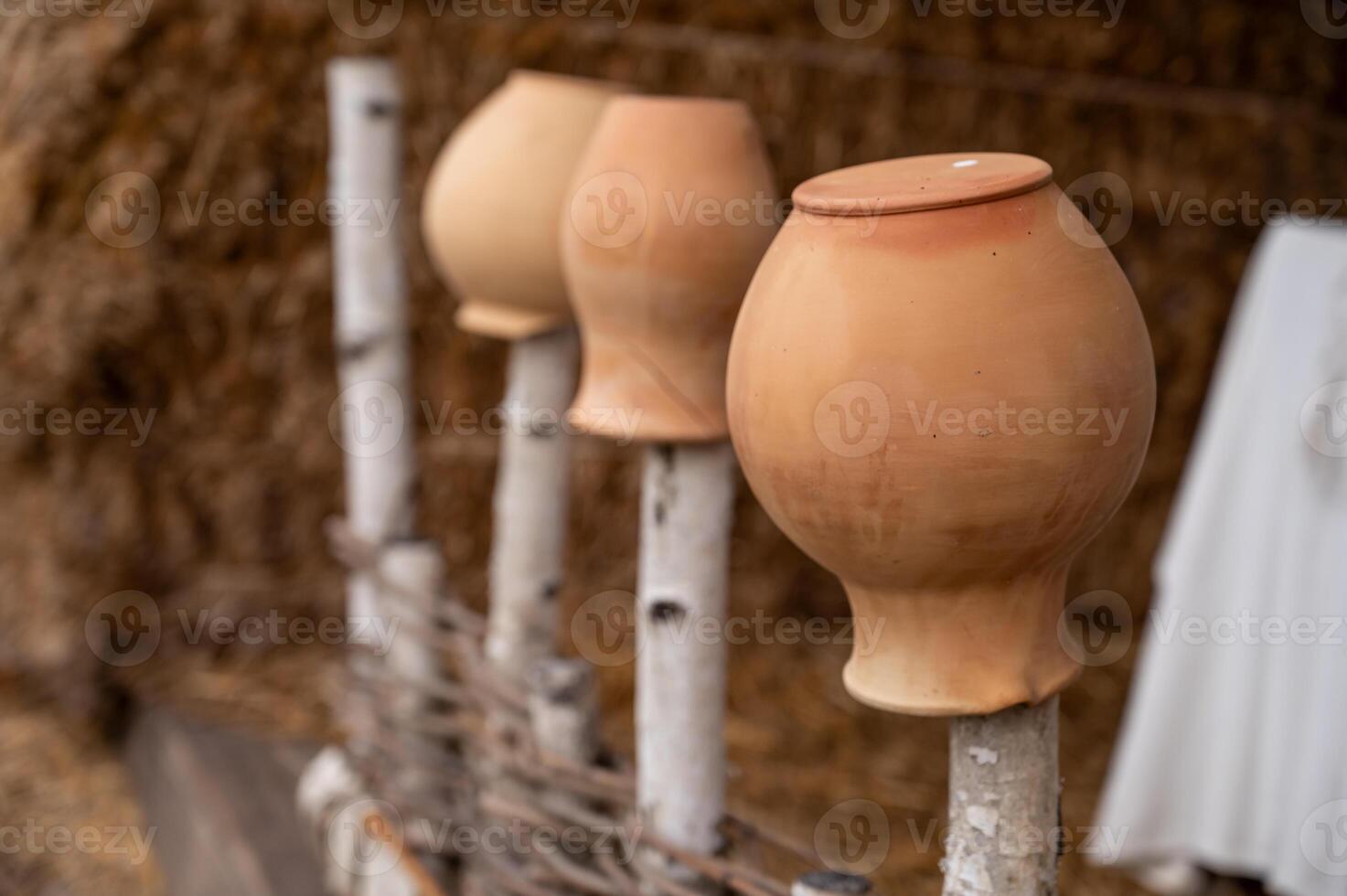 Three clay pots on sticks in front of a straw hut photo