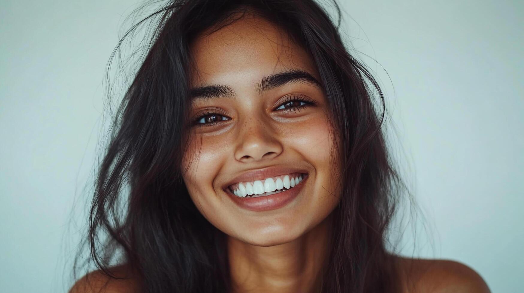 Radiant portrait of a woman with a warm smile, showcasing natural beauty and confidence. Her dark hair and bright teeth create a striking contrast. photo