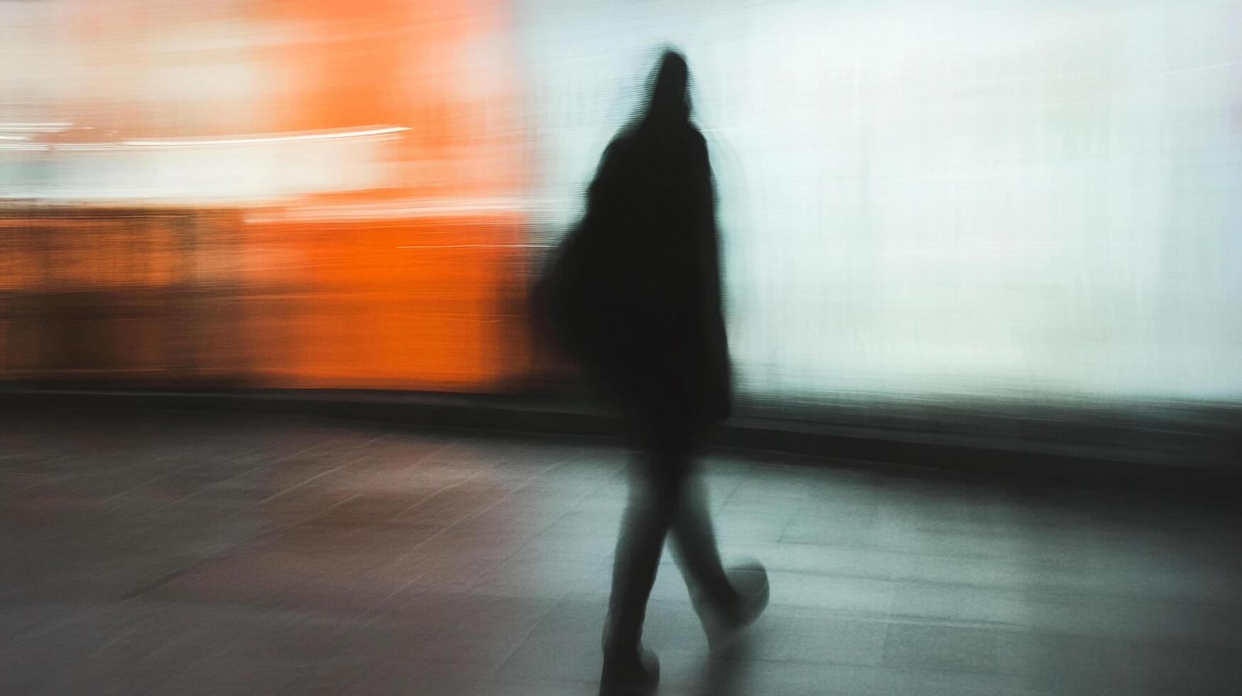 Motion blurred figure walking past a colorful background, giving an impression of pace and transience in an urban landscape. photo