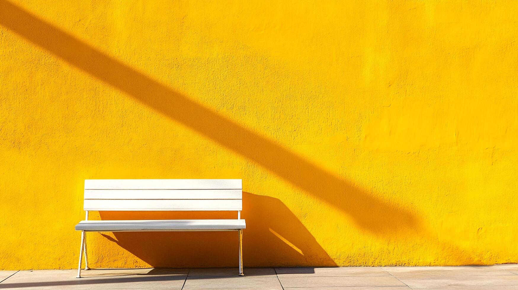 A stark white bench sits in stark contrast against a textured yellow wall bisected by a long diagonal shadow on a sunny day. photo