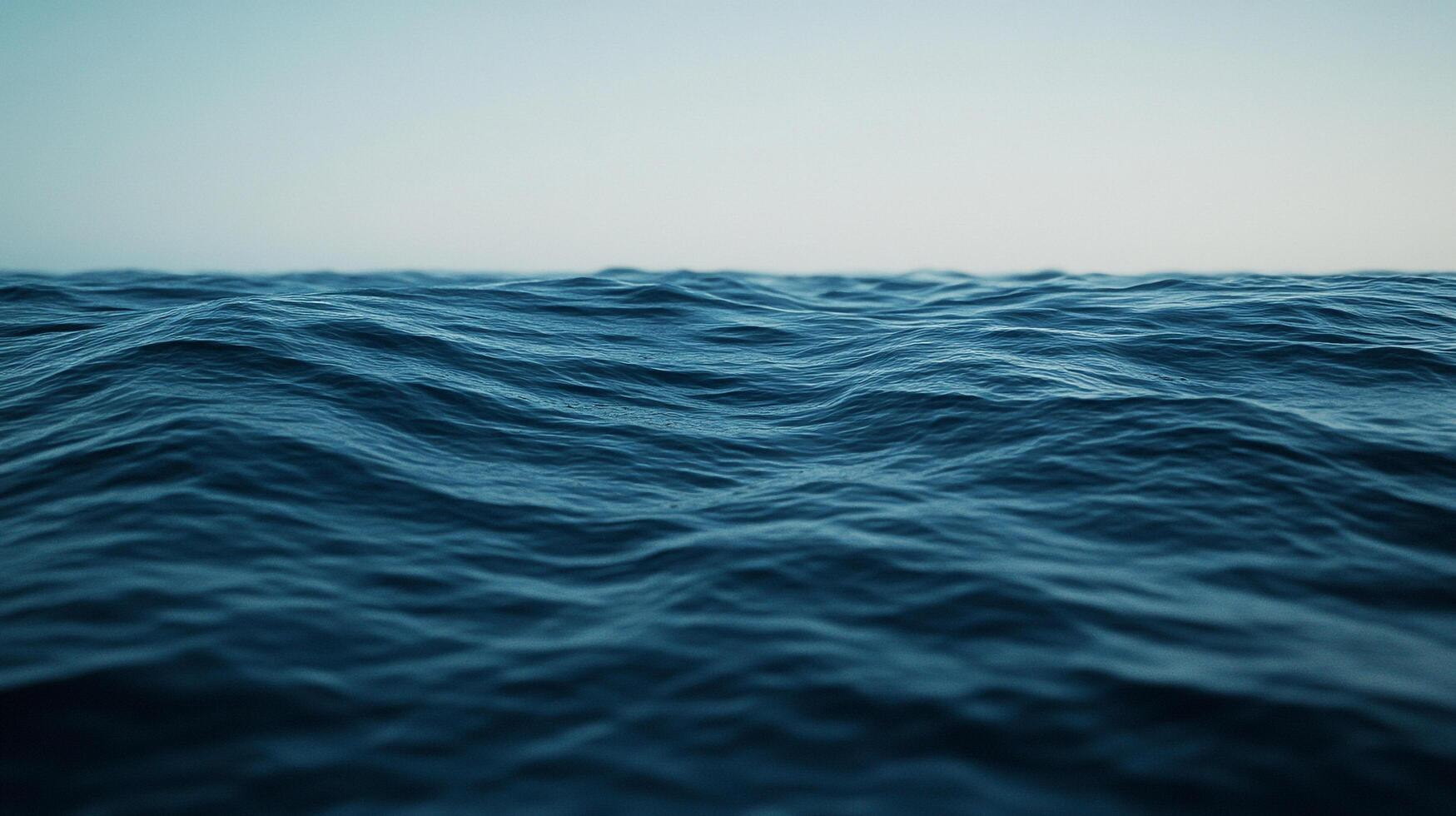 Open ocean view with gentle waves on a clear day, the water is a dark blue color with a light blue sky above the sea horizon. photo