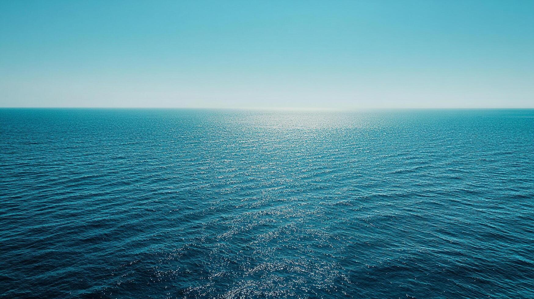 A calm ocean under a clear sky, the horizon blending seamlessly. Sunlight reflects on the water, creating a shimmering surface. photo