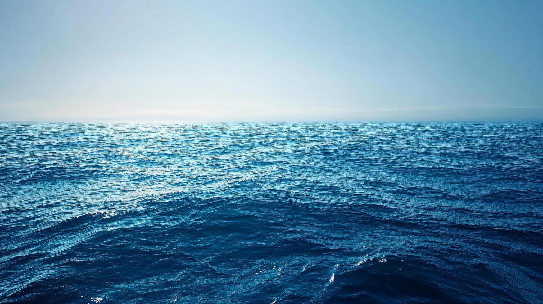 Vast expanse of deep blue ocean water meeting a clear light blue sky on the horizon. Gentle waves cover the ocean surface in the daytime. photo