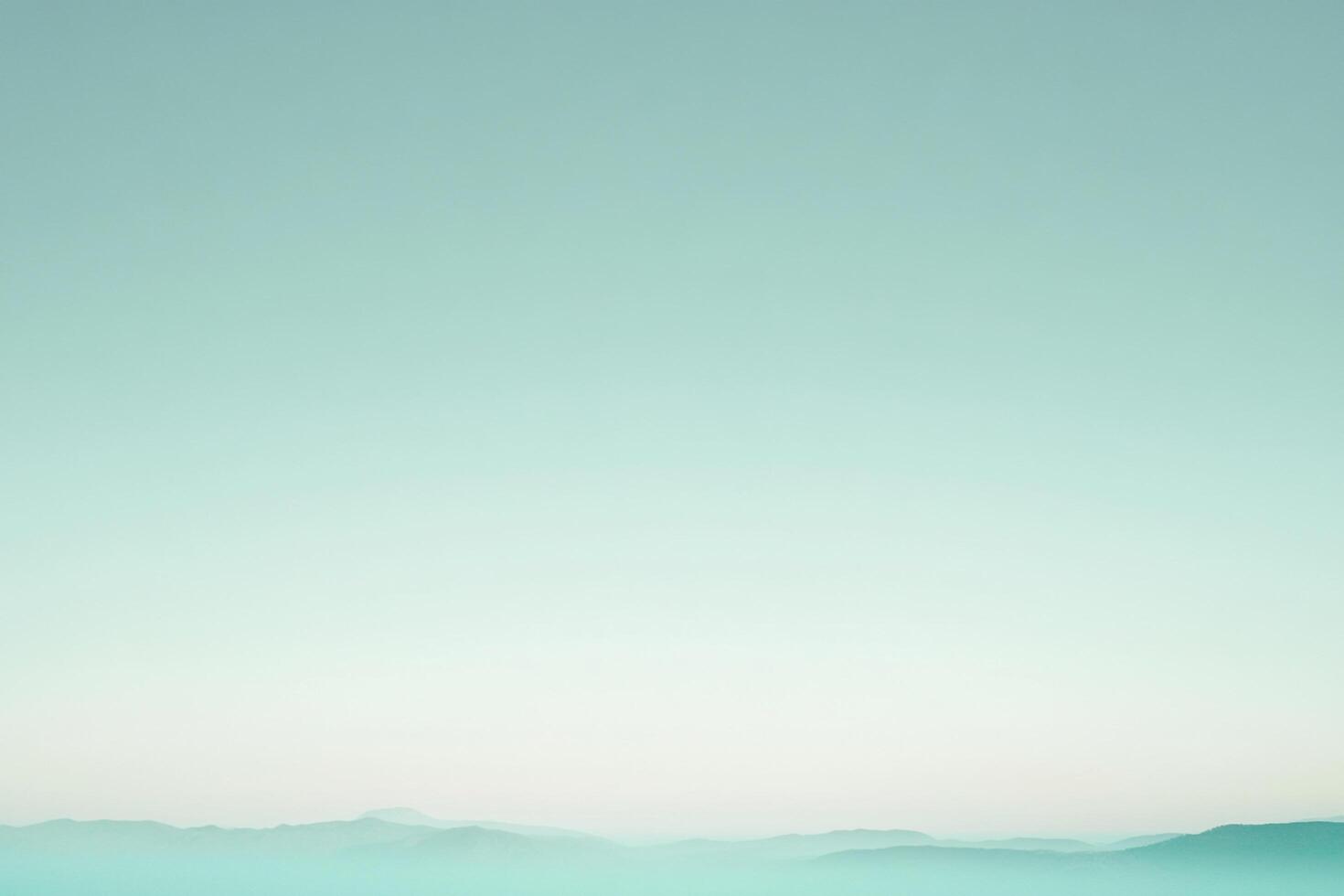 Turquoise-tinted landscape with softly diffused light, revealing mountain silhouettes veiled by a serene, hazy atmosphere. photo
