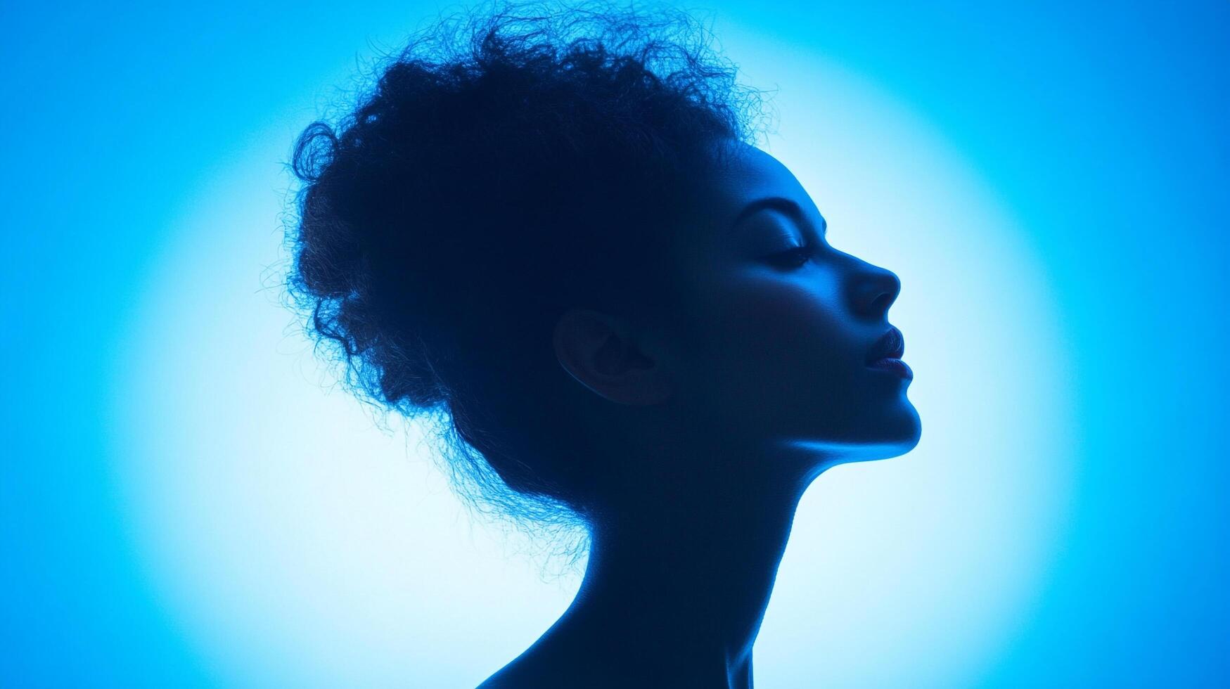 Portrait of a woman in blue light. The woman is serene and relaxed. The background is a gradient of blue. She has curly hair, her eyes are closed. photo
