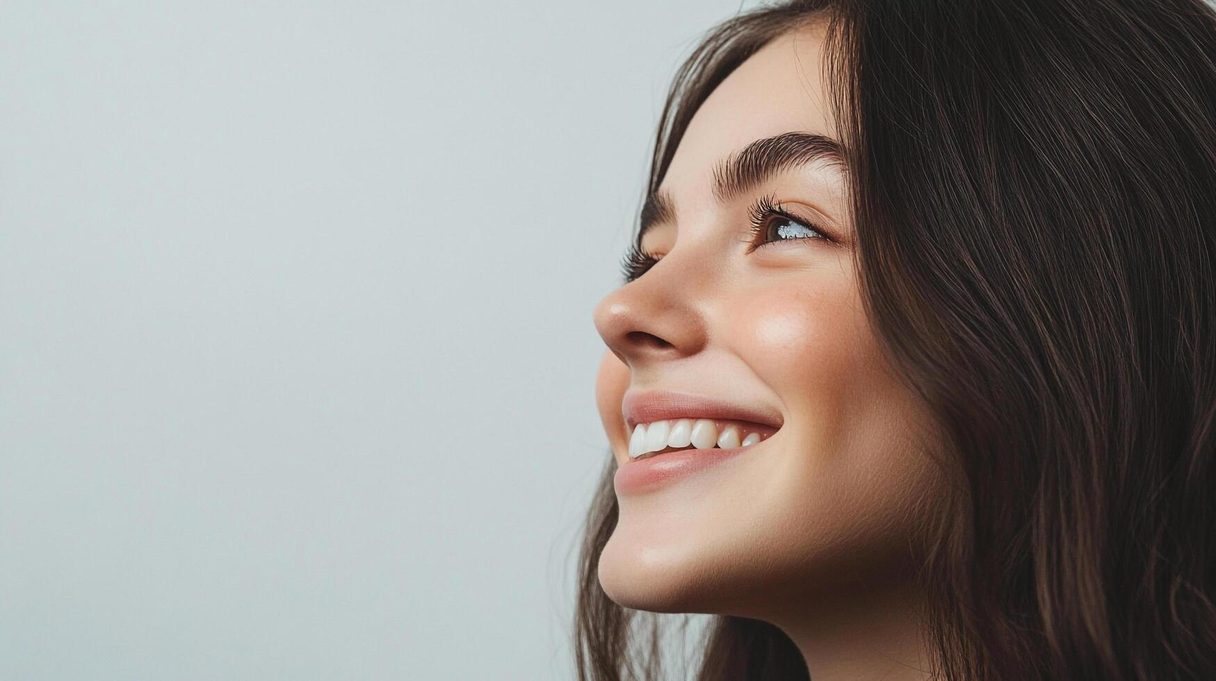 Radiant smile of a woman with brown hair looking upward, showcasing healthy skin and perfect teeth in a bright and cheerful composition. photo