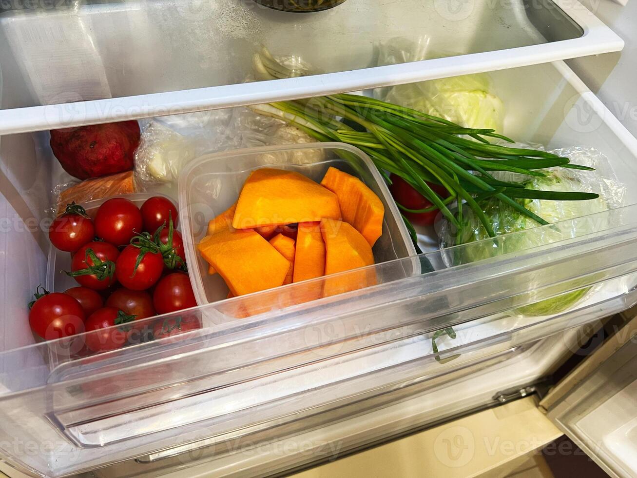 Fresh vegetables stored in the refrigerator drawer including tomatoes and pumpkin pieces photo