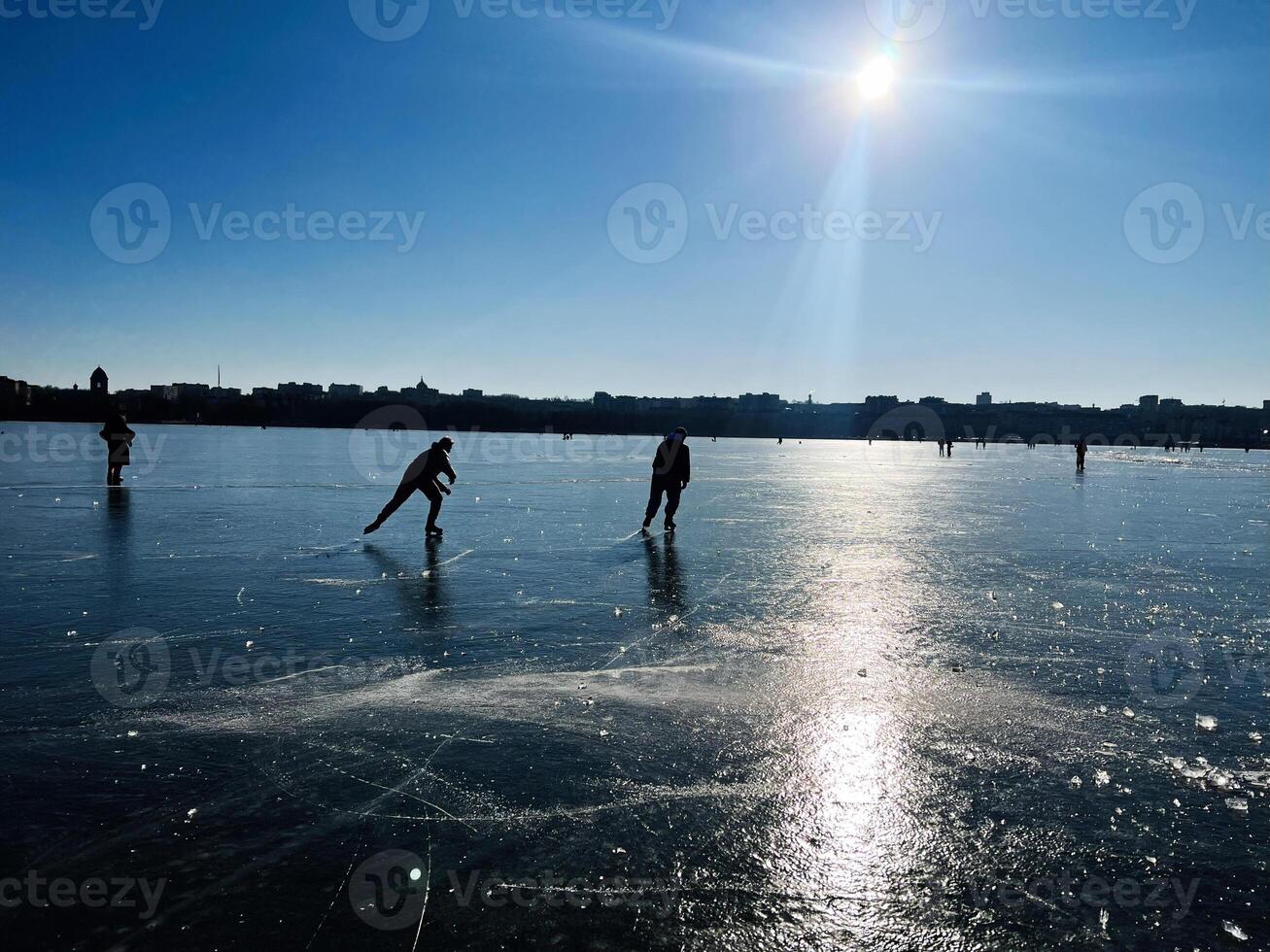 People ice skating on a frozen lake under bright sunlight and blue sky photo