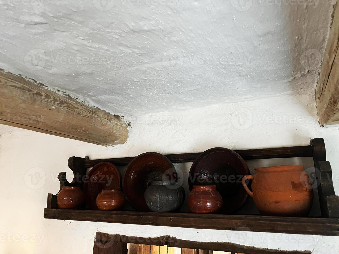 Rustic clay pots and plates displayed on a wooden shelf in vintage interior photo