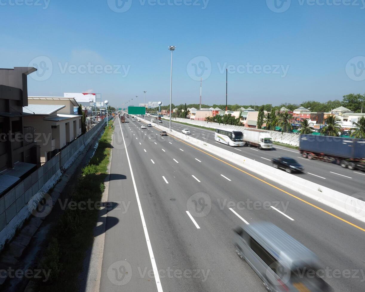 busy highway with vehicles in motion, surrounded by buildings and greenery photo