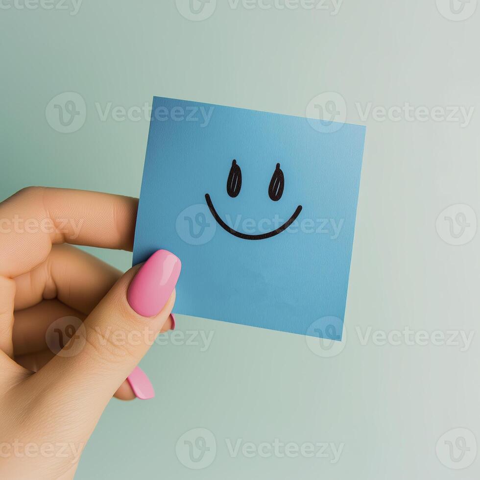 hand holding blue sticky note with smiling face emoji, conveying positivity and joy photo