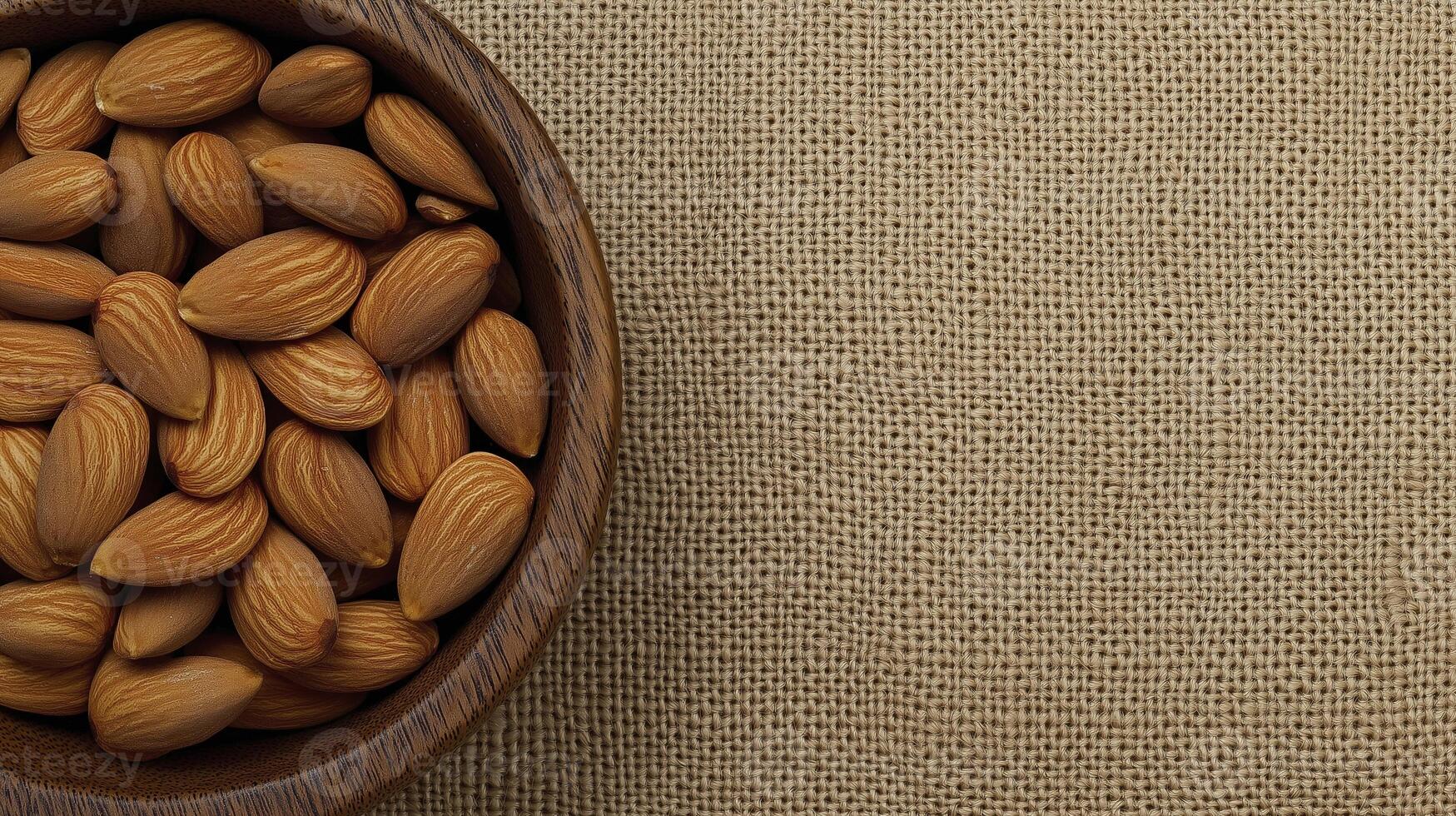 Fresh almonds in wooden bowl on textured jute background create warm, inviting scene photo