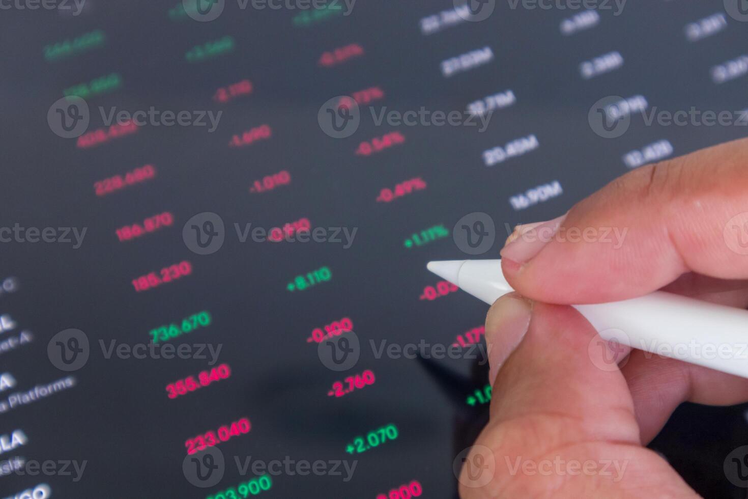 Businessman holding a pen pointing to stock market financial data interface on digital screen photo
