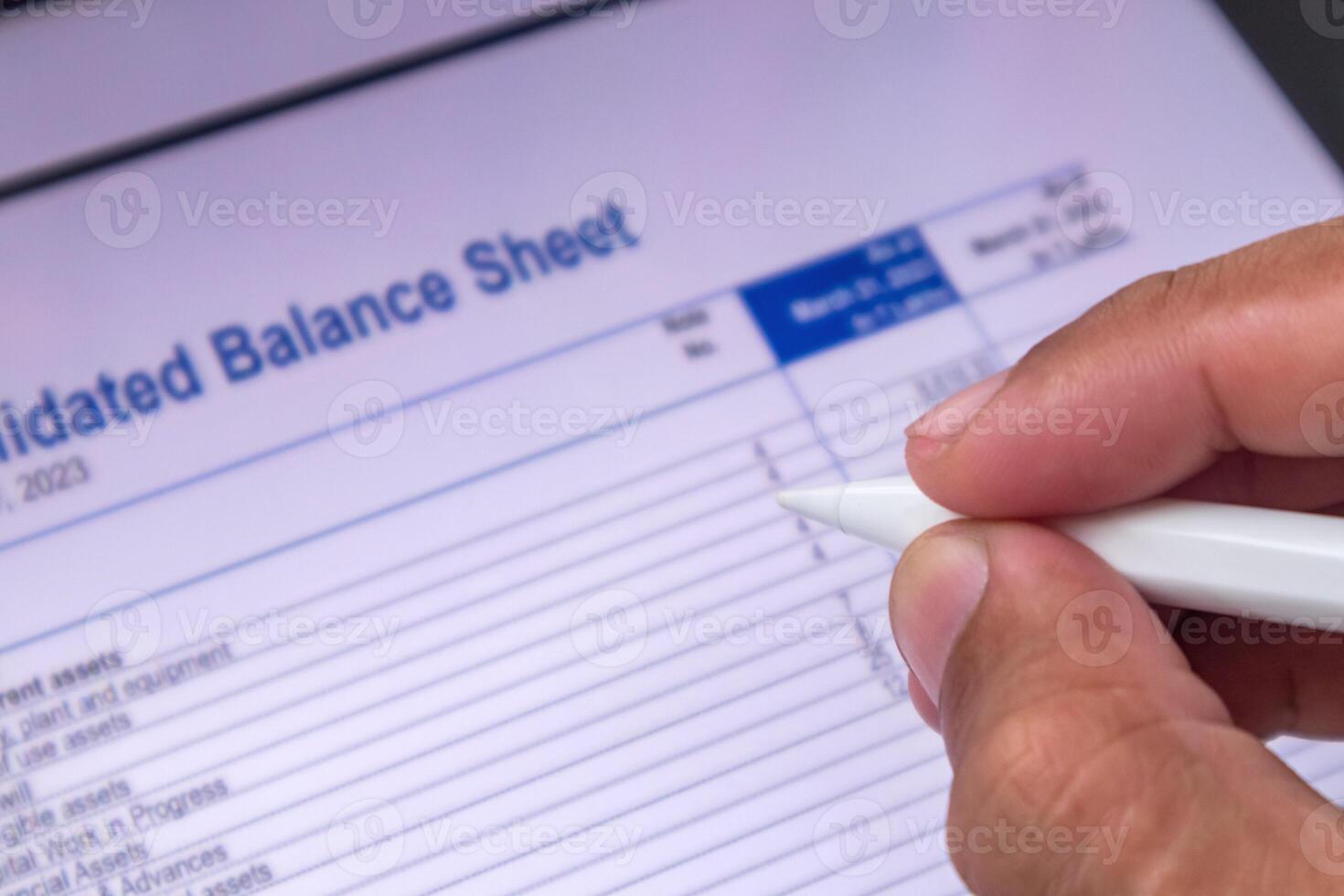 An accountant analyzing Balance sheet report data. Hand holding a pen and reviewing financial data on digital screen. photo