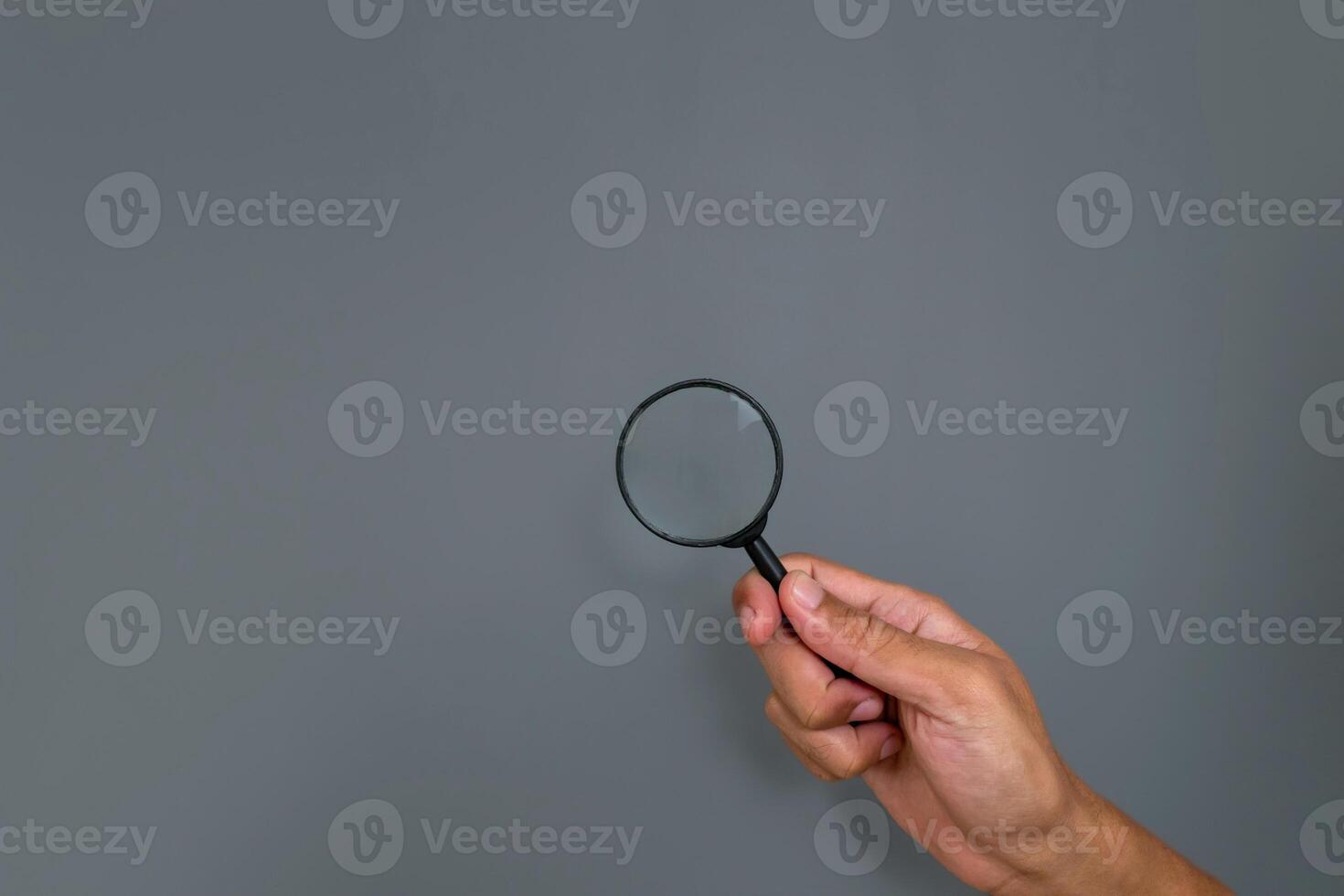 Man's hand holding a magnifying glass with copy space on a gray background photo