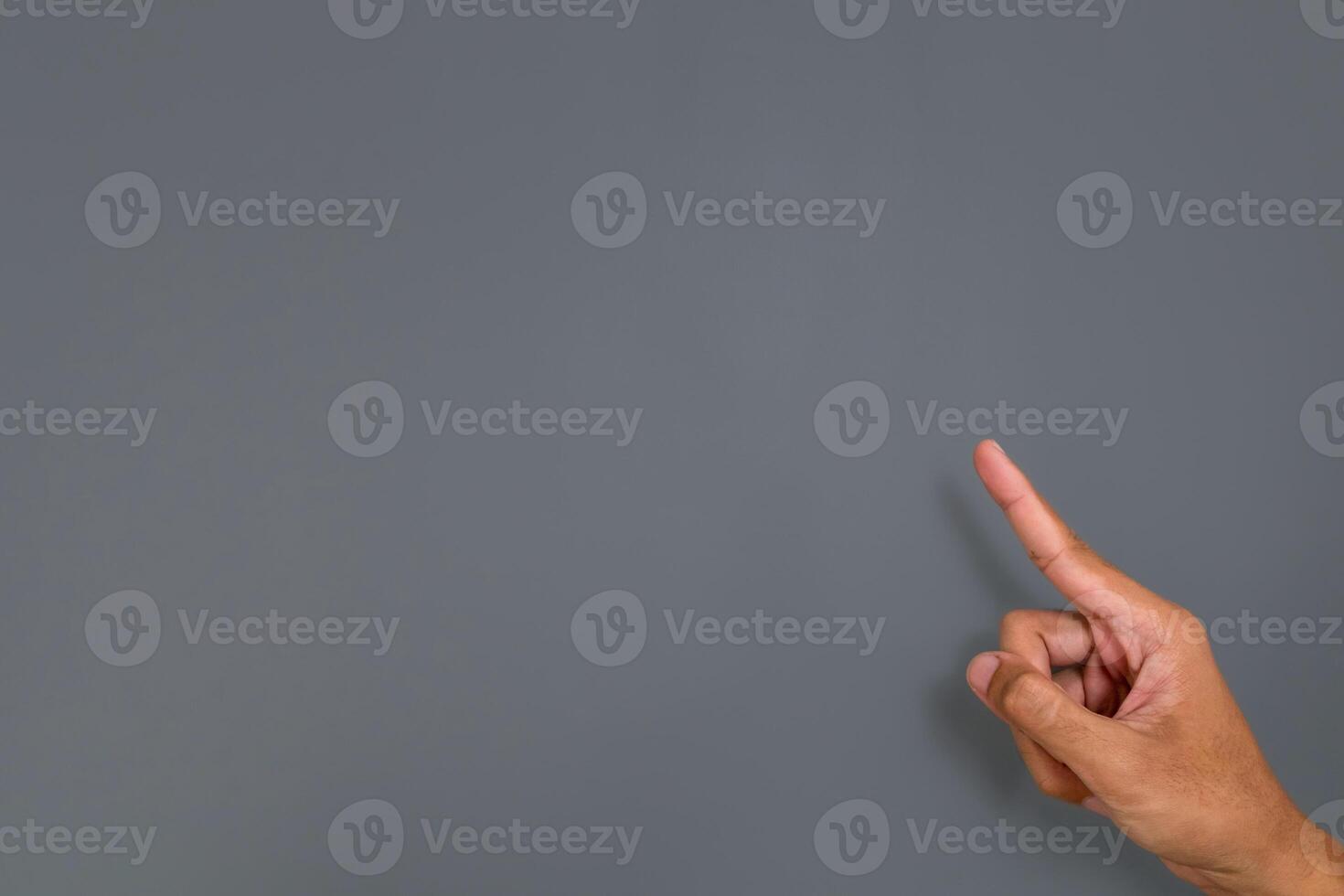 A man's hand with a pose or gesture pointing with index finger at something on a gray background photo