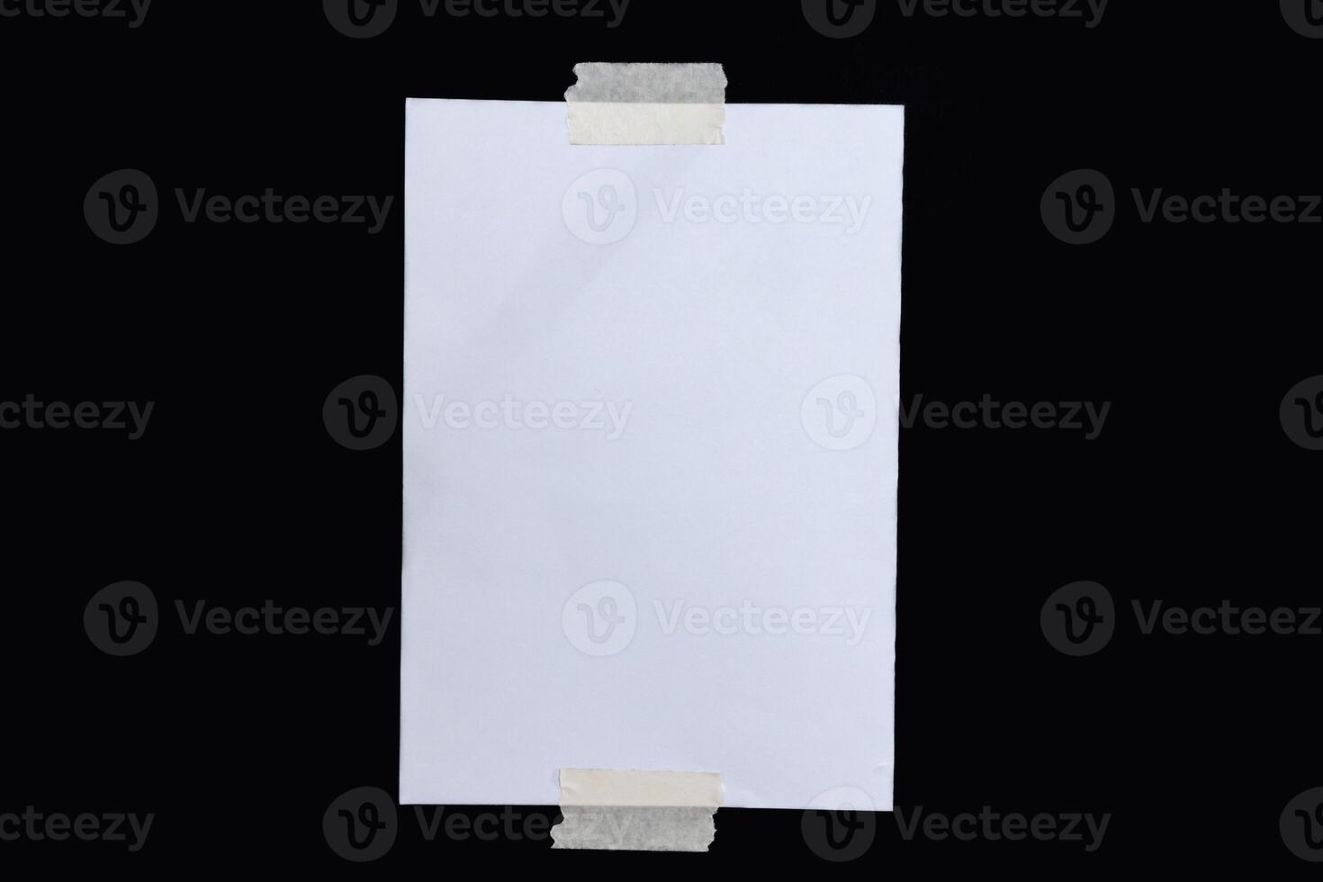Blank note paper for writing a message attached with tape on a black background photo