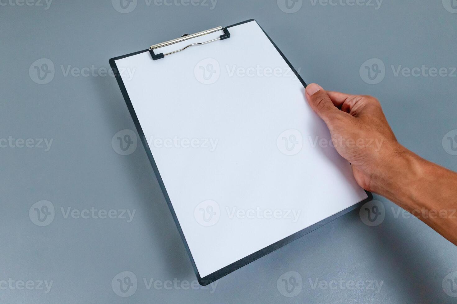 Hand holding a clipboard with blank white paper on gray background photo