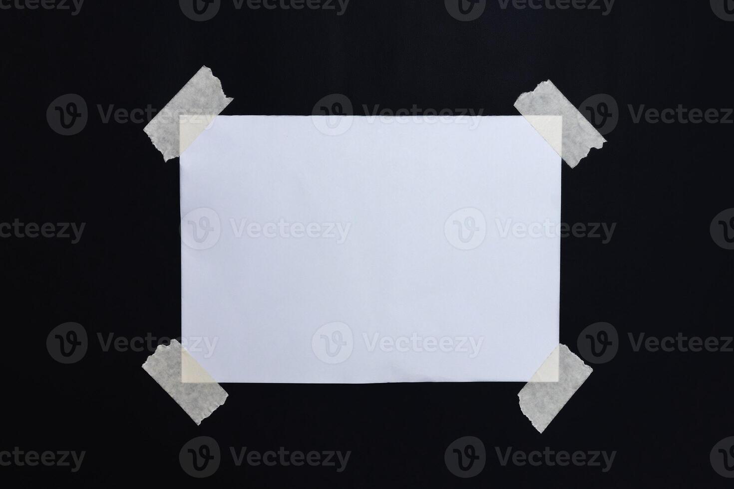 Blank note paper for writing a message attached with tape on all four sides on a black background photo