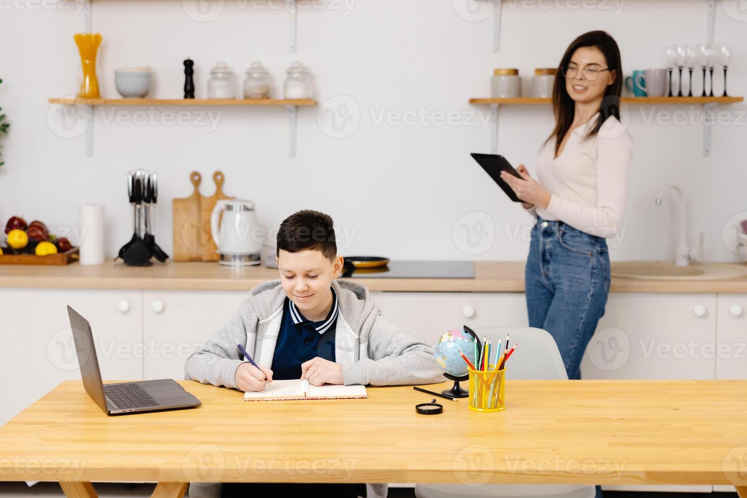 Woman helps a boy with his lessons using a tablet and a globe. A homeschooling student does his homework with the help of a tutor photo