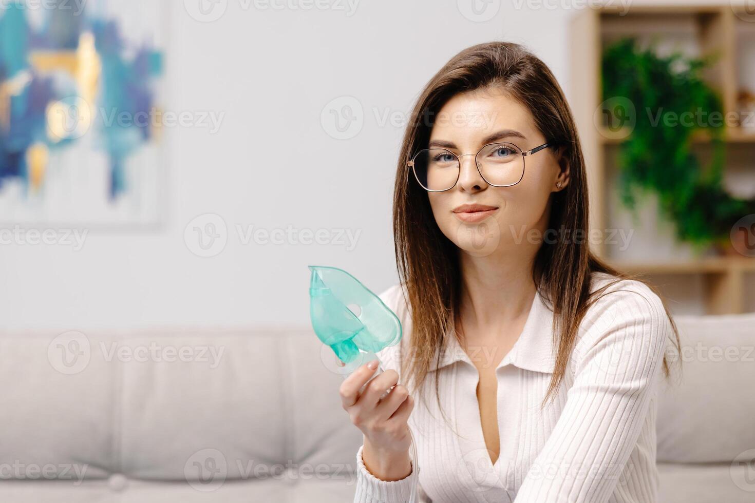 Woman holding a mask nebulizer inhaling fumes medication into lungs. Caucasian sick lady inhaling through inhaler mask at home. Self treatment of the respiratory tract using inhalation nebulizer photo