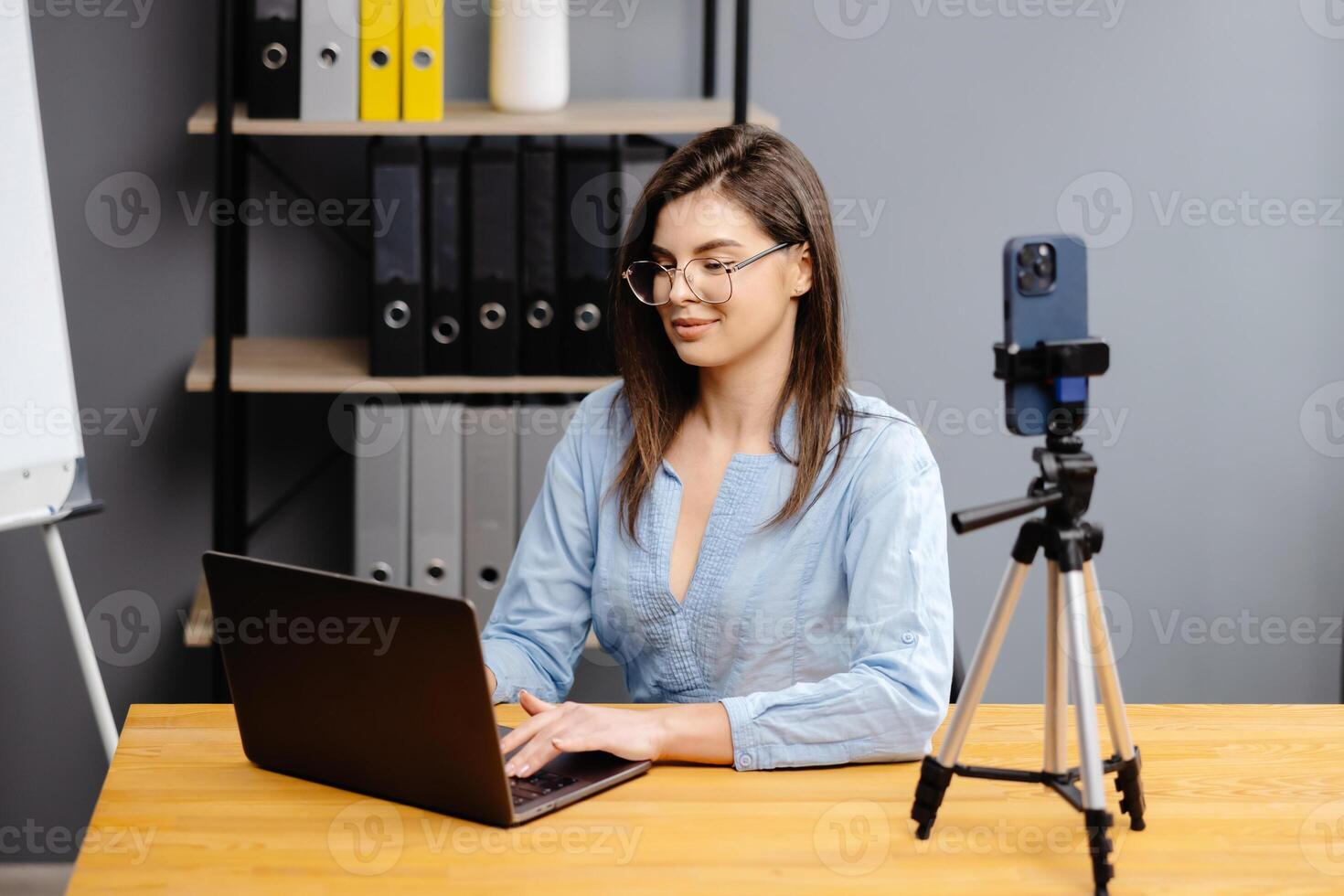 Videoconference And Training. Class of diverse students learning remotely online using web app. Female teacher providing lesson with laptop, recording on cellphone on tripod photo
