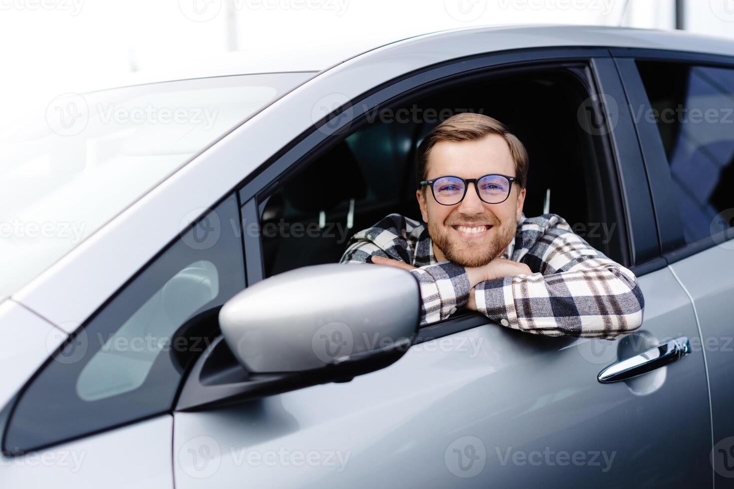 Man customer sitting in car salon and smiling, choosing auto and wanting to buy new automobile in showroom dealership store. Car sales concept photo